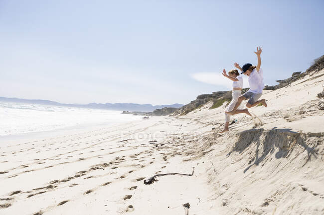 Two children leaping off sand dune on a beach — Stockfoto