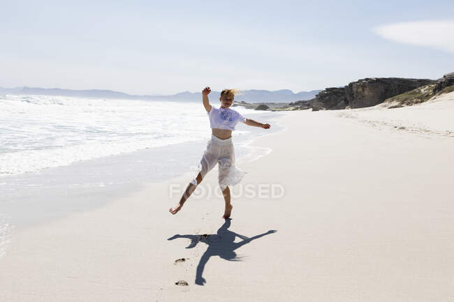 Teenage girl dancing alone on a sandy beach in South Africa by the water's edge — Foto stock