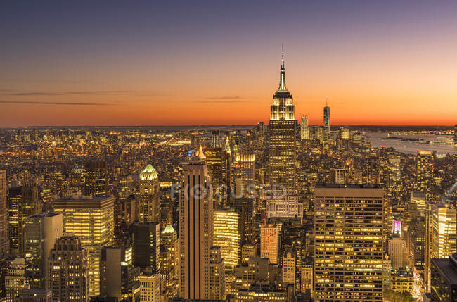 Empire state building rising above Manhattan skyline at sunrise or sunset. — Stockfoto