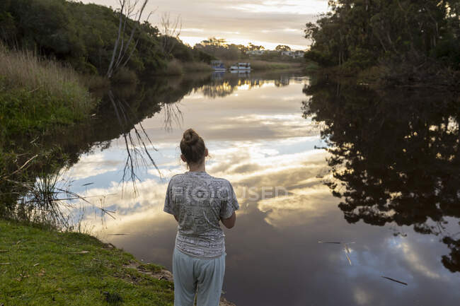 Teenage girl standing by a river at dusk. — Stock Photo