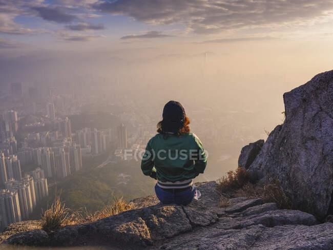 Frau sitzt auf Felsen in Hügeln über Hongkong und blickt auf die Stadt herab. — Stockfoto