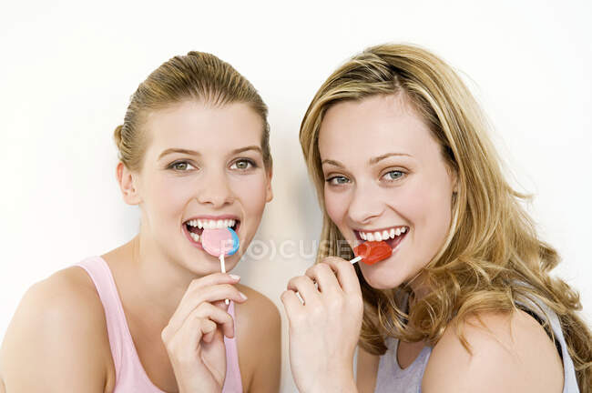 Dos mujeres comiendo piruletas y mirando a la cámara. - foto de stock