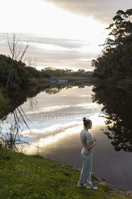 Ragazza adolescente in piedi vicino a un fiume al tramonto. — Foto stock
