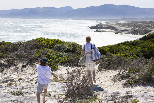 Девочка-подросток и младший брат с видом на пляж и скалистое побережье с волнами, разбивающимися на берегу. — стоковое фото