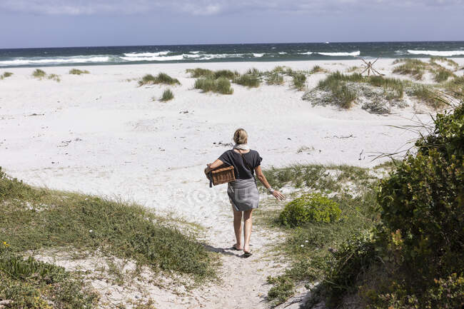 Femme adulte portant un panier de pique-nique sur Grotto Beach, Hermanus, Western Cape, Afrique du Sud. — Photo de stock