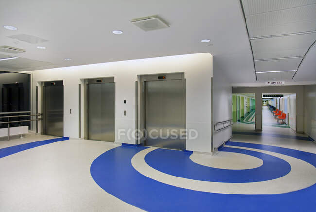 Ascensores en el atrio de un nuevo hospital moderno, patrones azules en el suelo - foto de stock