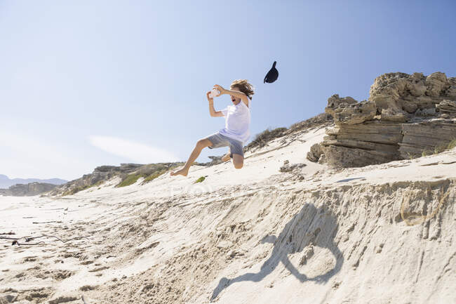 Um menino pulando de uma duna de areia na areia macia abaixo. — Fotografia de Stock