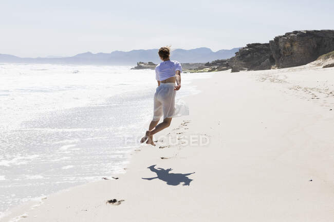 Ragazza adolescente che balla da sola su una spiaggia di sabbia in Sud Africa vicino al bordo dell'acqua — Foto stock