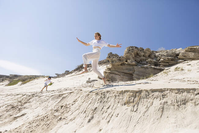 A teenage girl leaping from a sand dune into the soft sand below. — Stockfoto