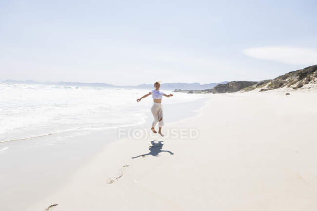 Ragazza adolescente che balla da sola su una spiaggia di sabbia in Sud Africa vicino al bordo dell'acqua — Foto stock