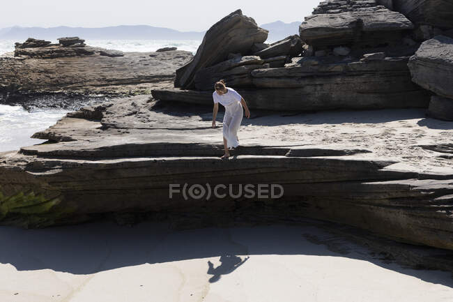 Девочка-подросток готовится спрыгнуть с гладкой плоской скалы над песчаным пляжем — стоковое фото