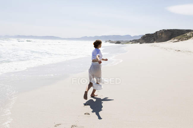 Adolescente bailando sola en una playa de arena en Sudáfrica por el borde del agua - foto de stock