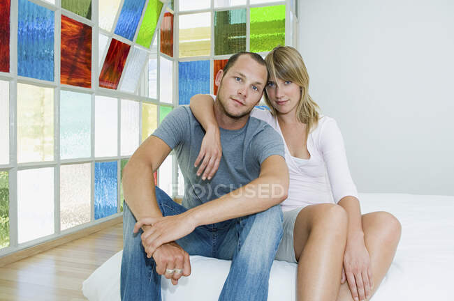 Чоловік і жінка сидять, обіймаючись на ліжку на ф'ючерсі барвистими скляними вікнами . — стокове фото