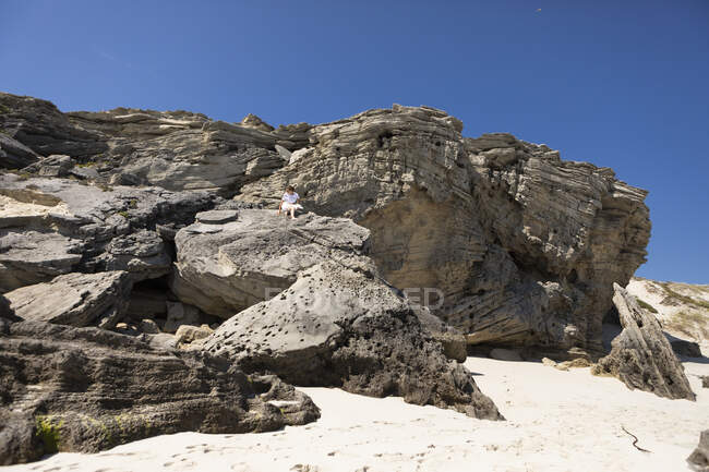 Girl sitting high up on a cliff on a sandy beach on the Atlantic Ocean coastline. — Stockfoto