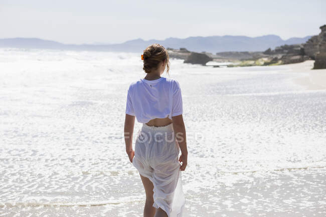 Teenage girl alone on a sandy beach in South Africa by the water's edge looking at the coastal view — Foto stock