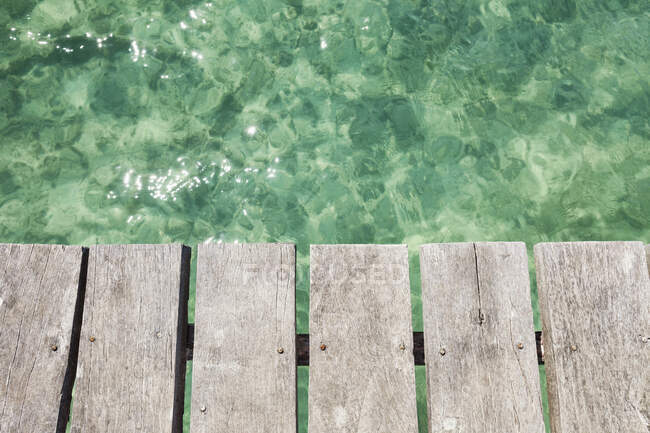 Muelle de madera sobre agua azul turquesa transparente poco profunda - foto de stock