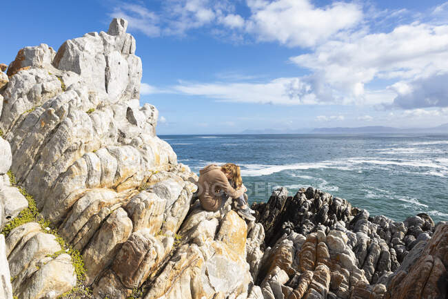 Девочка-подросток, сидящая на камнях с видом на Атлантический океан, ее голова лежит на коленях — стоковое фото