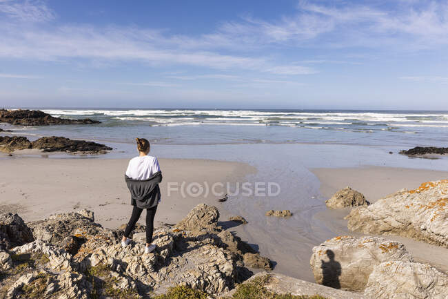 Adolescente de pé sobre rochas com vista para uma praia de areia — Fotografia de Stock