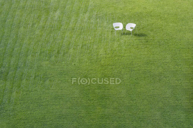 Two white office chairs on green lawn with pattern of stripes mown into grass meeting at a corner. — Photo de stock