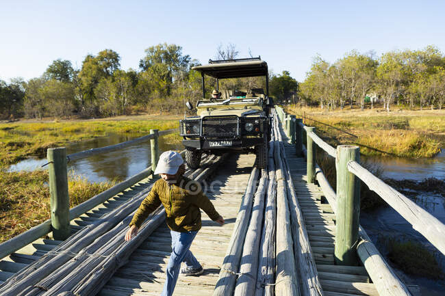 Un niño caminando a través de un puente de madera sobre pantanos. - foto de stock