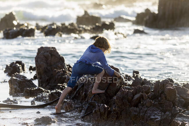 Junge spielt im Sand zwischen Felsen am Strand, Brandungswellen brechen, — Stockfoto