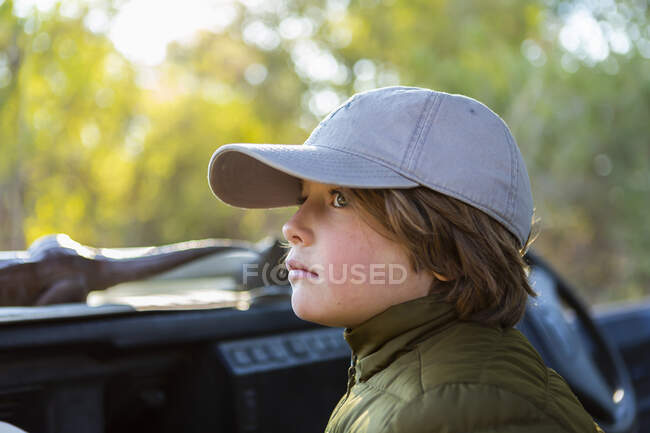Portrait of young boy in a baseball cap in a safari vehicle. — Stock Photo