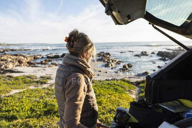 Donna adulta alla porta aperta di un veicolo in spiaggia prepararsi per l'escursionismo. — Foto stock