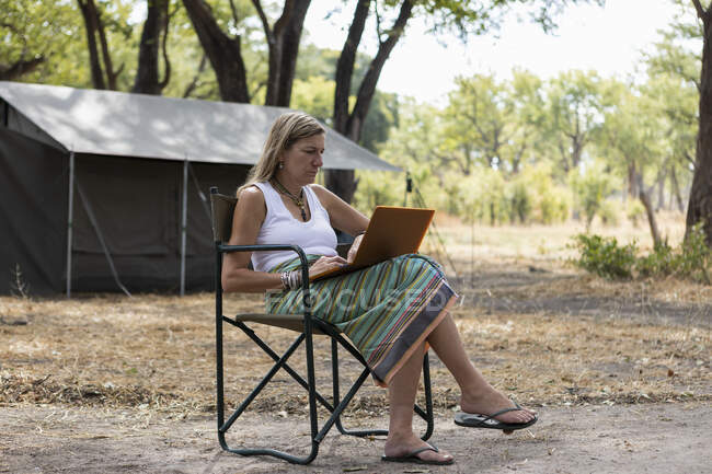 Mujer adulta usando laptop, campamento de tiendas de campaña, Delta del Okavango, Botswana - foto de stock