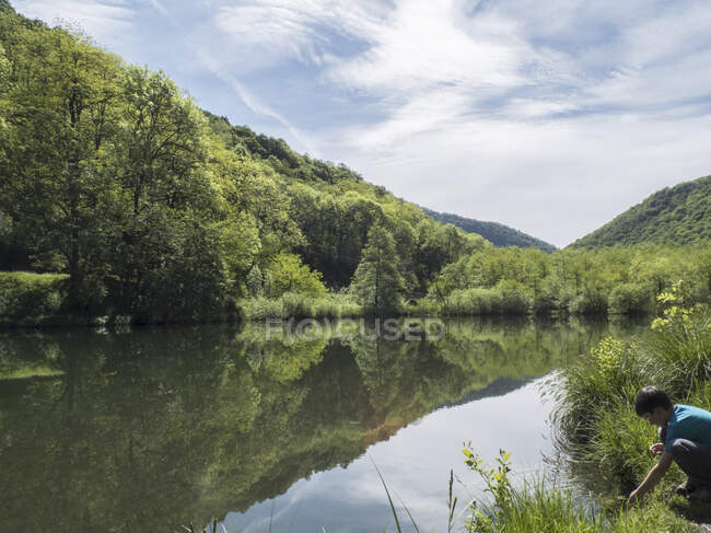Vista sobre el tranquilo lago de agua plana, montañas y bosques, un niño en la orilla. - foto de stock