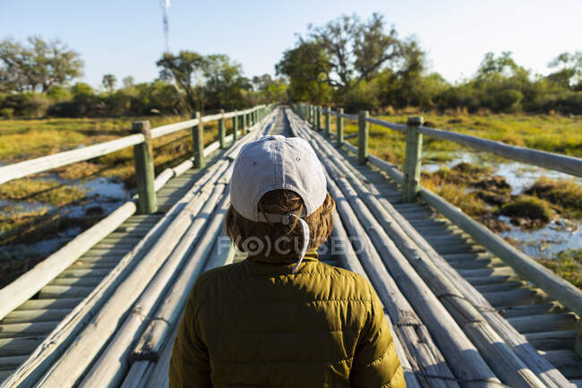Un ragazzo che cammina attraverso un ponte di legno sulla palude da solo — Foto stock