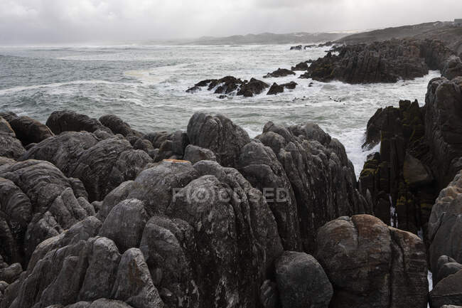 Zerklüftete Felsen und die felsige Atlantikküste am Strand von De Kelders, Wellen brechen an Land. — Stockfoto