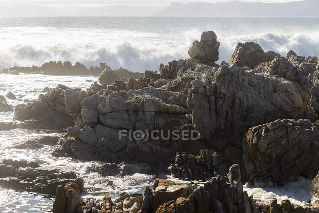 Zerklüftete Felsen am Ufer bei De Kelders, hohe Wellen rollen herein und brechen an den Felsen — Stockfoto