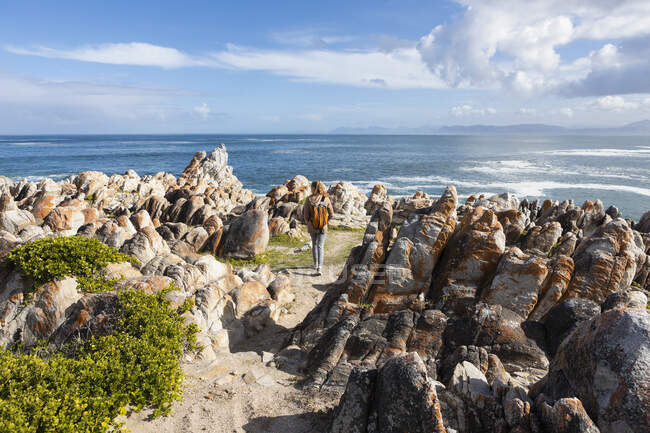Ragazza adolescente con uno zaino in piedi sulle rocce guardando sopra l'oceano — Foto stock