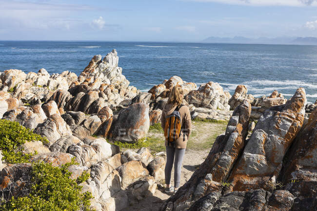 Дівчинка - підліток з рюкзаком, що стоїть на скелях і дивиться через океан. — стокове фото