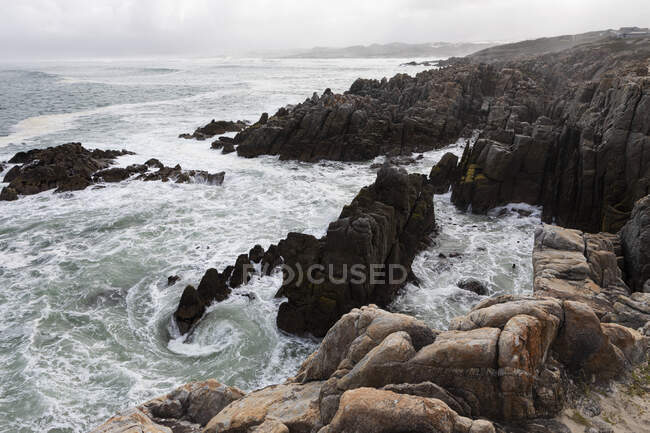 Rocas dentadas y la costa rocosa del Atlántico en la playa De Kelders, olas rompiendo en la orilla. - foto de stock