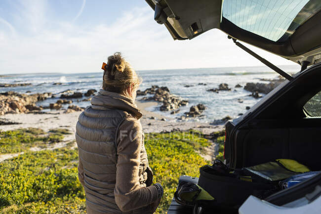 Adult woman by the open door of a vehicle at the beach getting ready for hiking. — Stock Photo