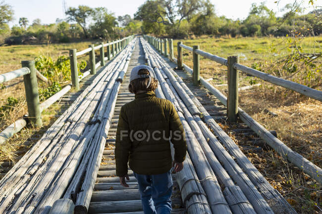 A boy walking across a wooden bridge over marshland alone — Stock Photo
