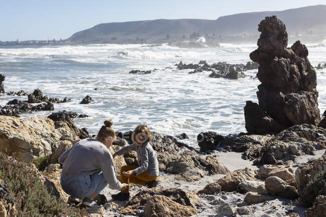 Adolescente e um menino explorando as rochas e surfar, mar traste levantando-se das ondas quebrando do oceano. — Fotografia de Stock