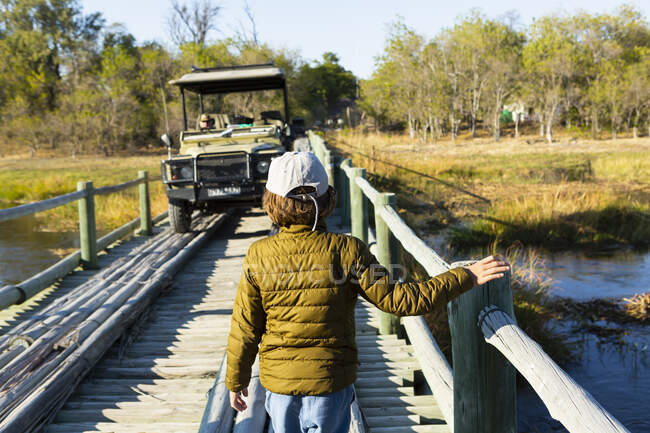 Un niño caminando a través de un puente de madera sobre pantanos. - foto de stock