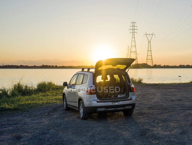 Auto mit offenem Kofferraum mit Blick auf einen See oder eine Bucht bei Sonnenuntergang. — Stockfoto