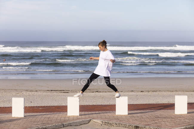 A teenage girl balancing on posts on a sandy beach. — Stock Photo