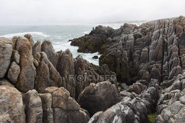 Rocas dentadas y la costa rocosa del Atlántico en la playa De Kelders, olas rompiendo en la orilla. - foto de stock