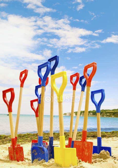 Colourful childrens' spades stuck in sand on beach. — Stock Photo
