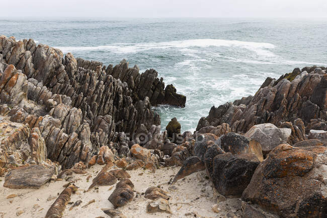 Rochas irregulares e o litoral rochoso do Atlântico na praia De Kelders, ondas que quebram na costa. — Fotografia de Stock