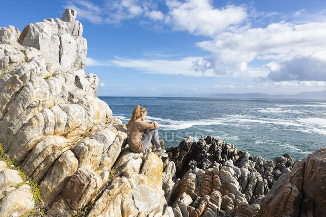 Дівчинка - підліток сидить на скелях і дивиться на Атлантичний океан і узбережжя. — стокове фото