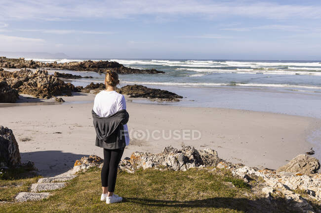 Девочка-подросток, стоящая на скалах с видом на песчаный пляж — стоковое фото