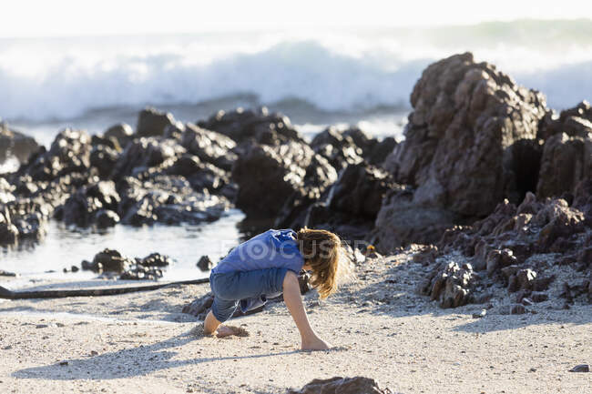 Мальчик играет на скалистом пляже, держа длинную нить водорослей — стоковое фото