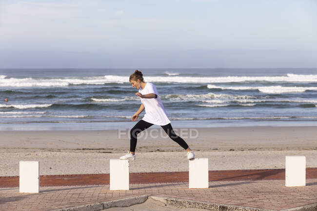 A teenage girl balancing on posts on a sandy beach. — Stock Photo