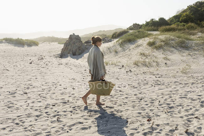 Adolescente caminando a lo largo de la arena llevando una cesta. - foto de stock