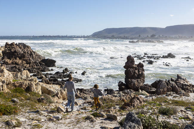 Adolescente y un niño explorando las rocas y el surf, el traste del mar levantándose de las olas rompientes del océano. - foto de stock
